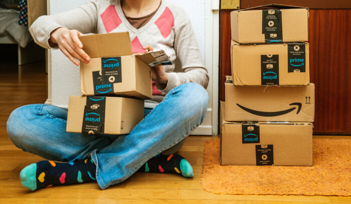 Frau sitzt lächelnd auf dem Boden und öffnet Amazon Pakete